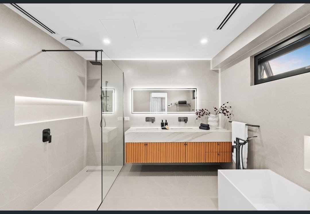 Bathroom with a timber vanity, illuminated mirror and frameless glass shower.